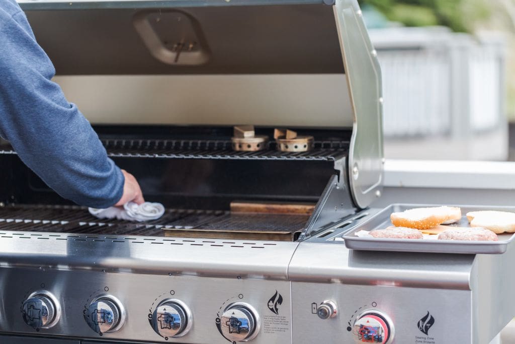 Person wiping stainless steel grill grates with a cloth to demonstrate how to clean a grill before cooking.