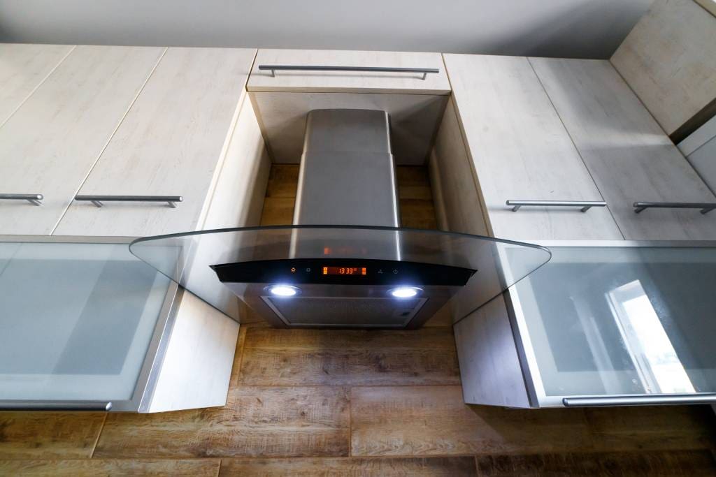 Contemporary kitchen with a stainless steel range hood vent installed through the ceiling, showing completed ceiling-mounted ventilation above a cooktop.